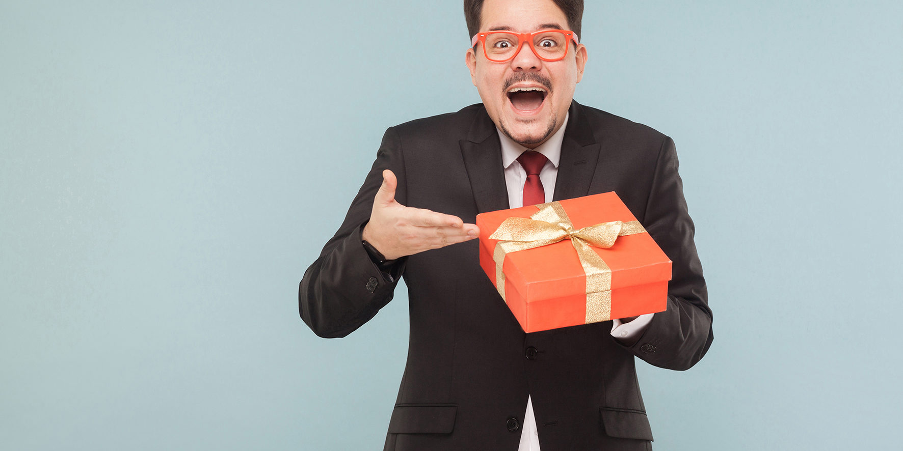 Happy man in black suit holding red gift box and looking at camera with excited face.