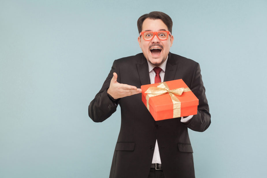 Happy man in black suit holding red gift box and looking at camera with excited face.