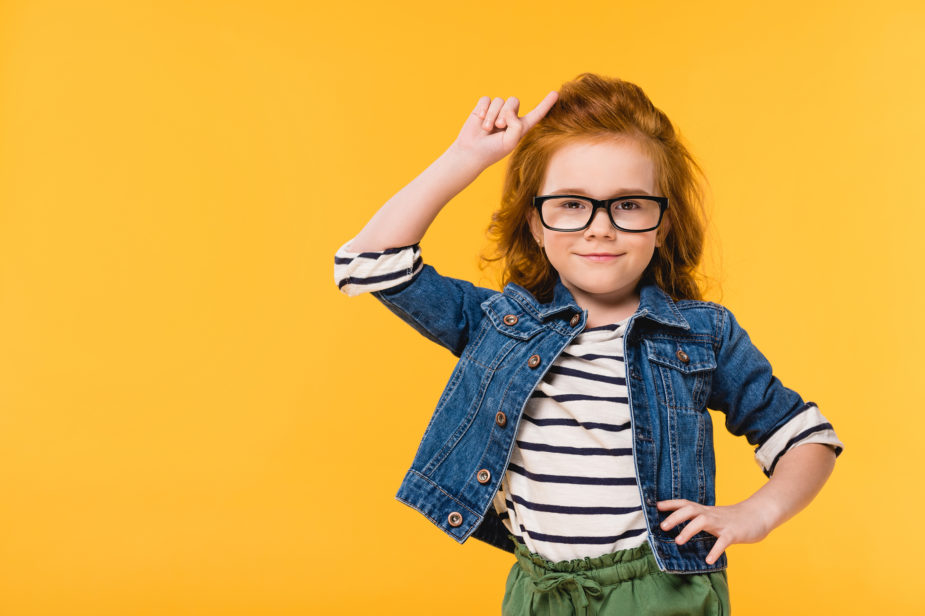 portrait of cute little kid in eyeglasses standing akimbo isolated on yellow